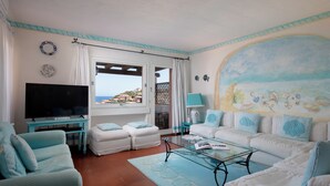 A living room with a TV, white sofas, a glass coffee table, and a mural of the sea. - Cerbiatta al Molo Apartments by Wonderful Italy (Arzachena)