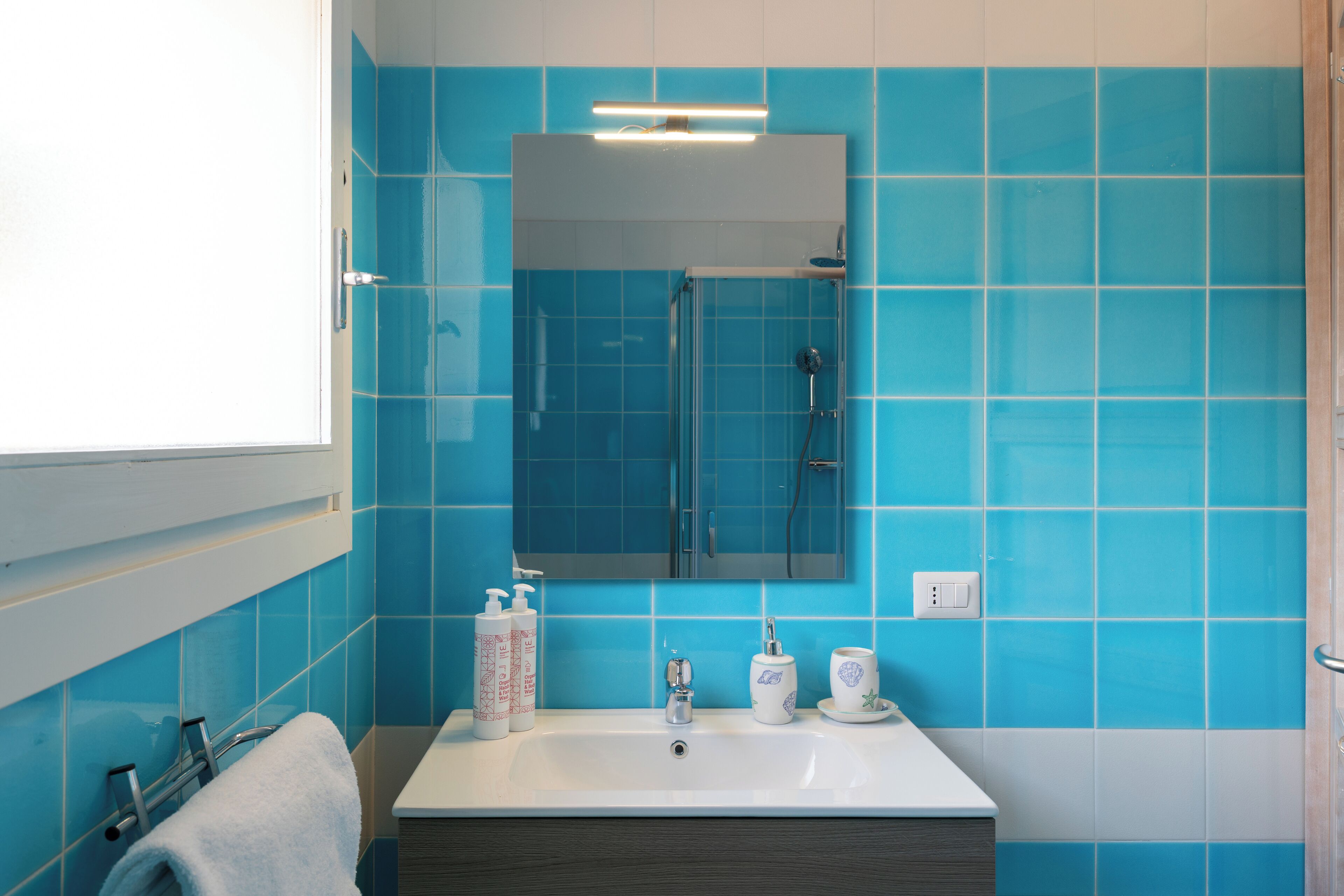 Une salle de bain avec un lavabo blanc, des carreaux bleus, un miroir et un porte-serviettes.