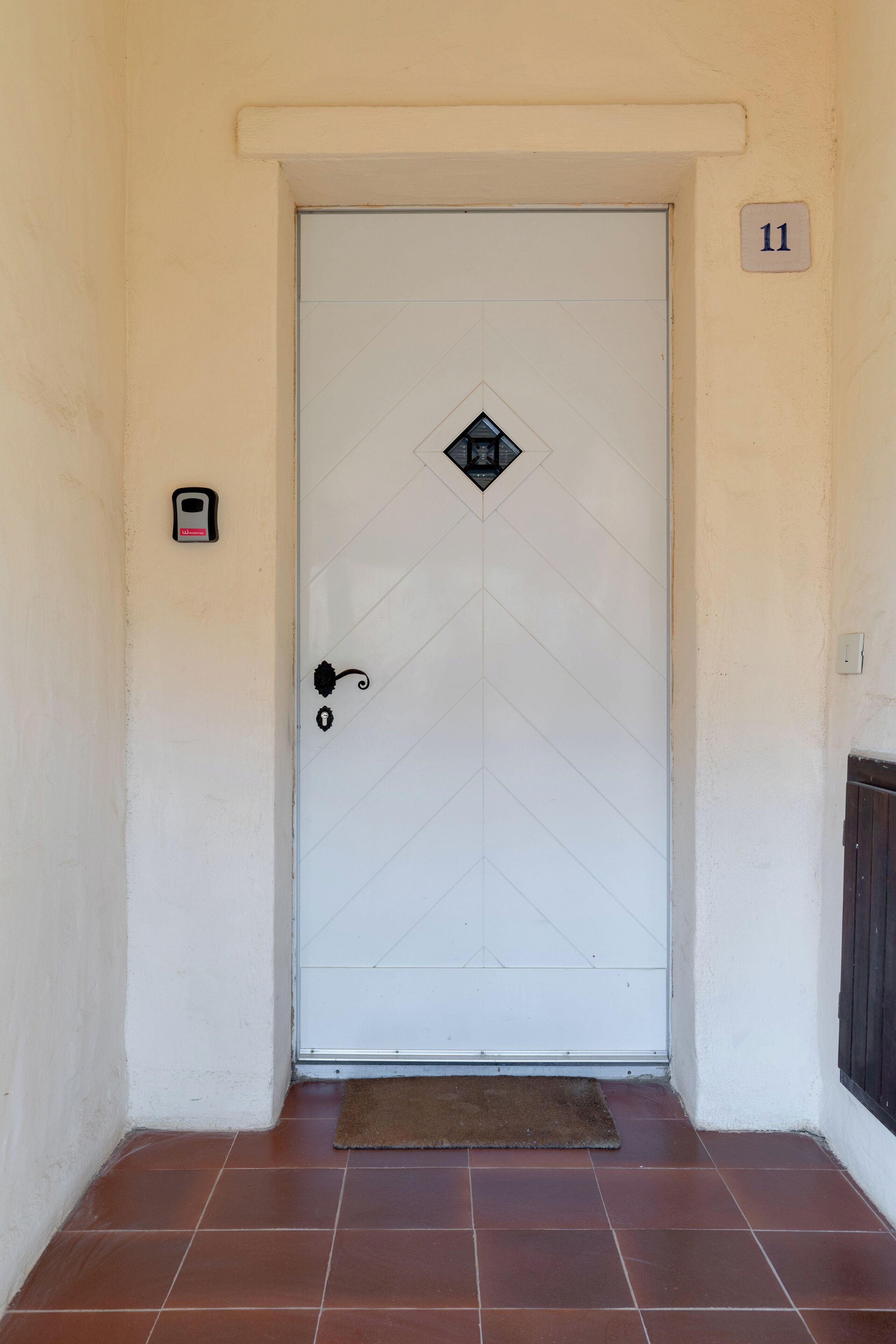 Une porte blanche ornée d’une serrure dont le trou est en forme de losange et d’un petit verrou. Au-dessus de la porte, on peut voir une plaque avec le numéro « 11 ».