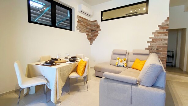 Un coin repas avec une table dressée pour quatre personnes, un canapé avec des coussins, un mur décoratif en briques et un grand miroir.