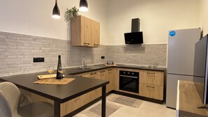 Une cuisine moderne avec un plan de travail foncé, des meubles en bois, un four encastré et un réfrigérateur.