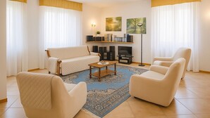 Un salon comprenant un canapé, deux fauteuils, une table basse, un tapis, une cheminée et des œuvres d’art accrochées au mur.