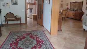 Un vaste salon agrémenté d’un grand tapis rouge à motifs, d’un banc en bois et d’un coin repas avec un buffet en bois et des chaises.