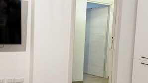 A room with a flat-screen TV mounted on the wall, a bench, and a door leading to another room.