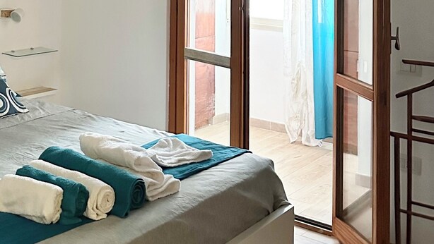 A bedroom with a bed, a glass door leading to a balcony, and a white air conditioning unit on the wall.