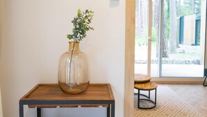 On aperçoit clairement une pièce avec une table en bois, un vase en verre contenant une plante et une grande fenêtre donnant sur l’extérieur.