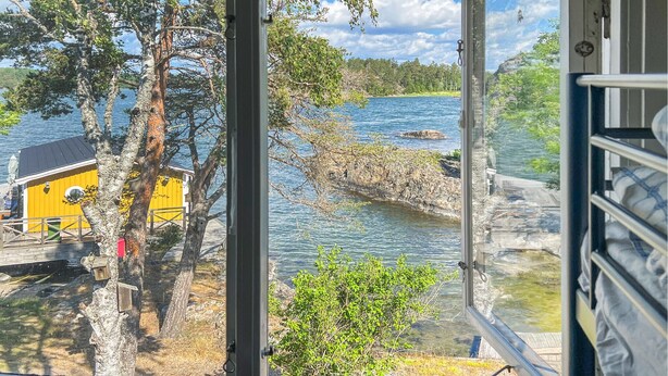 A view from inside a cabin overlooking a lake with a yellow building and trees. - 4 bedroom amazing home in Sorunda (Sorunda)