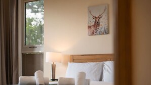 Ein Hotelzimmer mit einem Bett, einer Lampe, einem Bild von einem Reh und einem Fenster mit Jalousien.