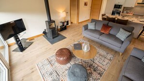 Ein modernes Wohnzimmer mit Sofa, Couchtisch und Hocker, einem Kamin und einer Küche im Hintergrund.
