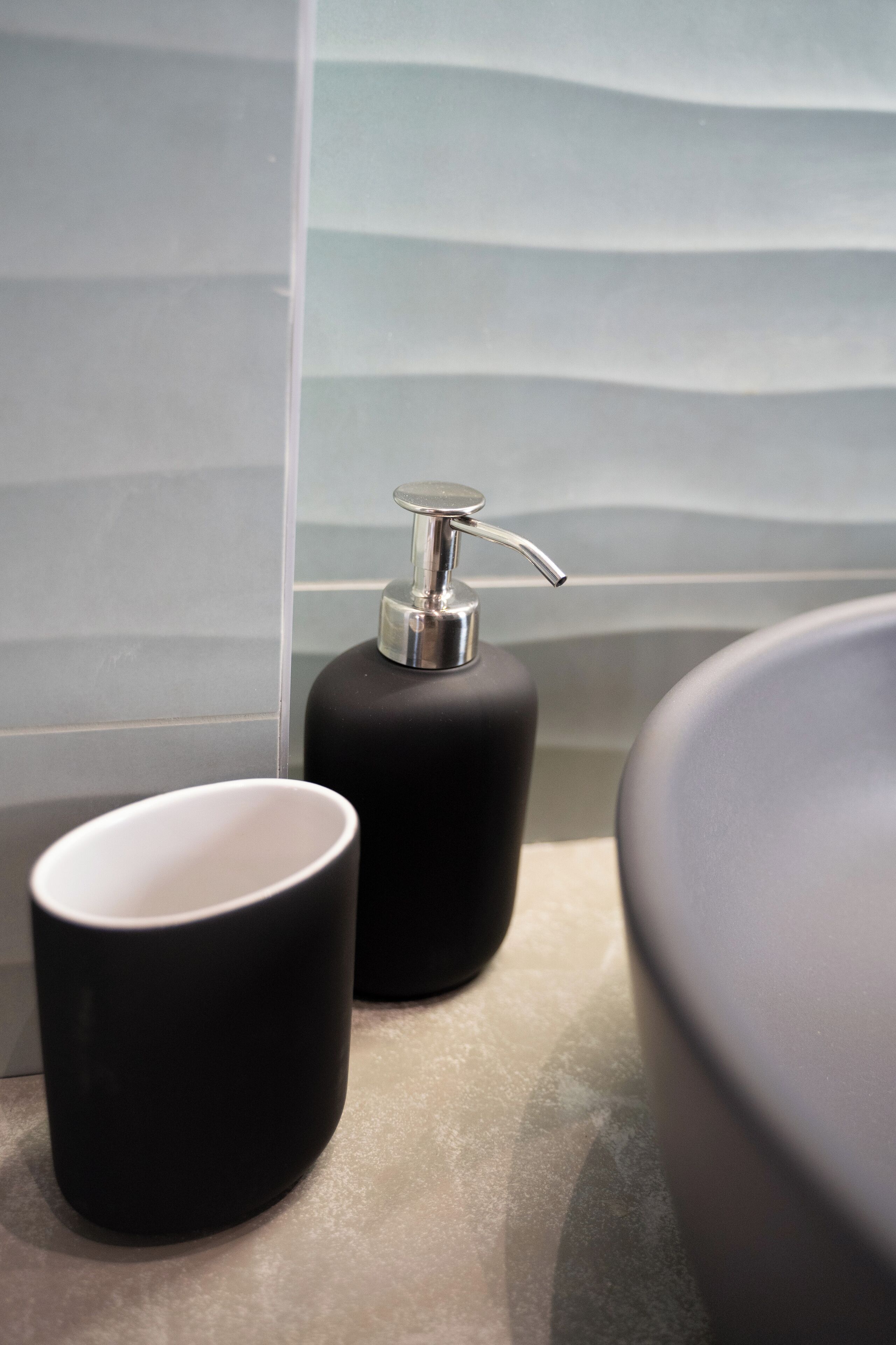 Ein Badezimmer mit modernem Design, das einen schwarzen Seifenspender und eine weiße Tasse auf der Arbeitsfläche zeigt.