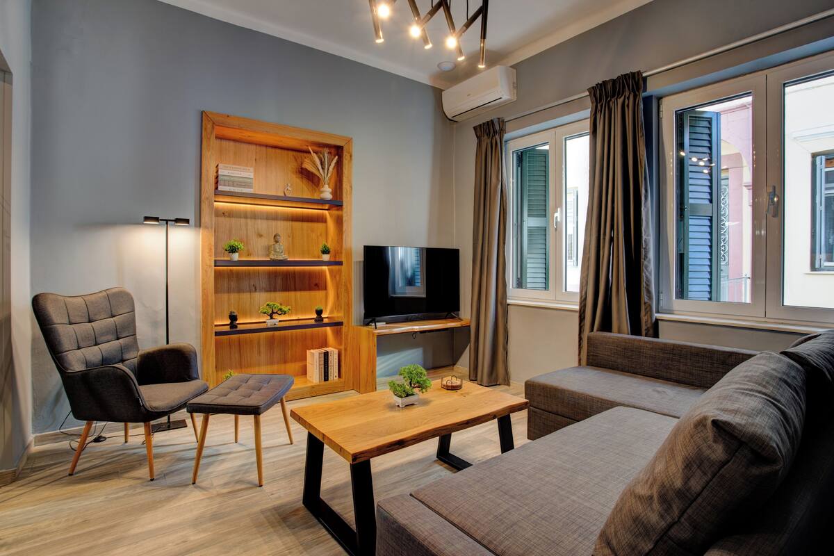 Un salon moderne comprenant un canapé, un fauteuil, une table basse, un téléviseur et une bibliothèque en bois.