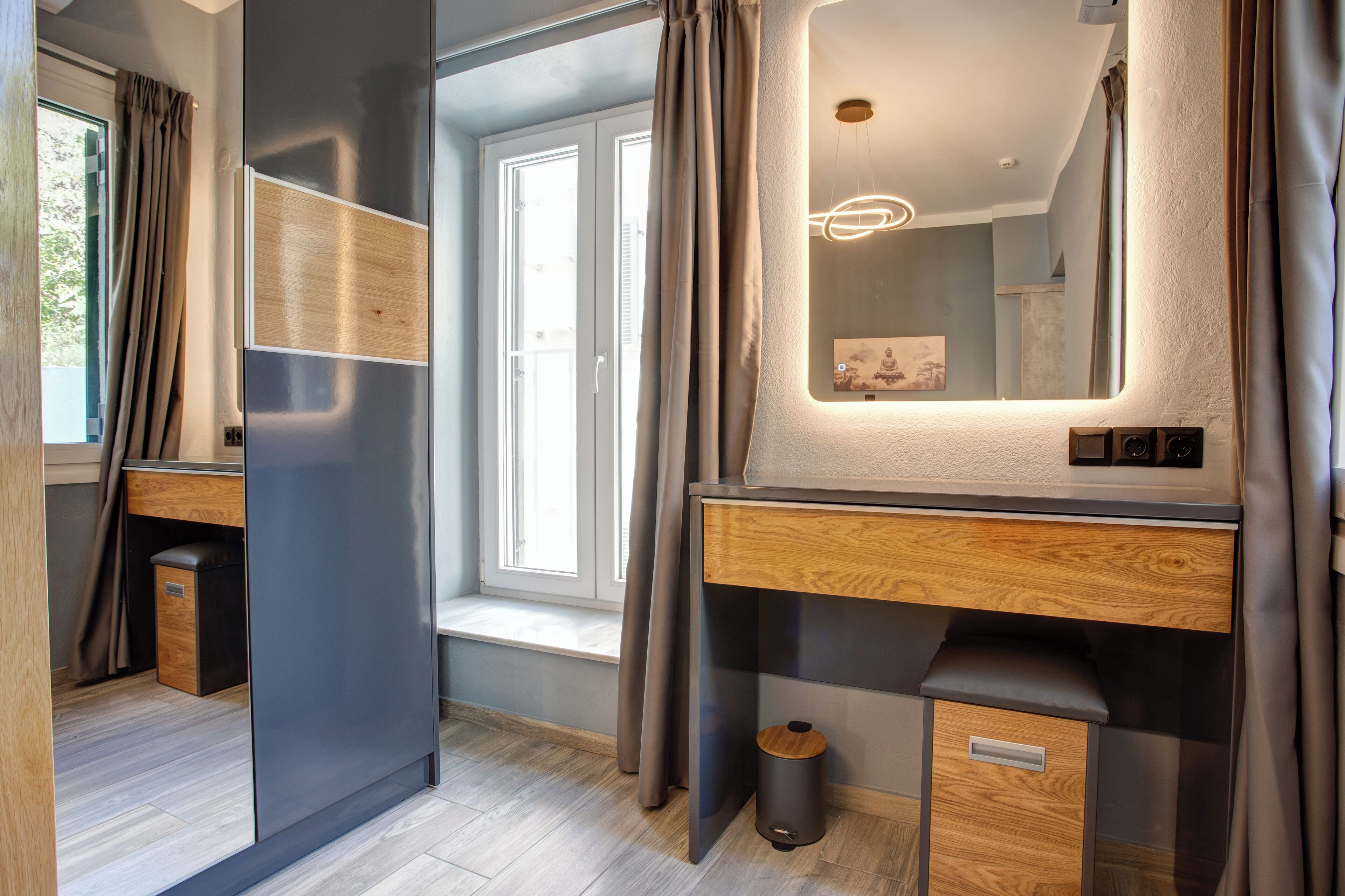 A modern bathroom with a large mirror, wooden vanity, and a small trash bin.