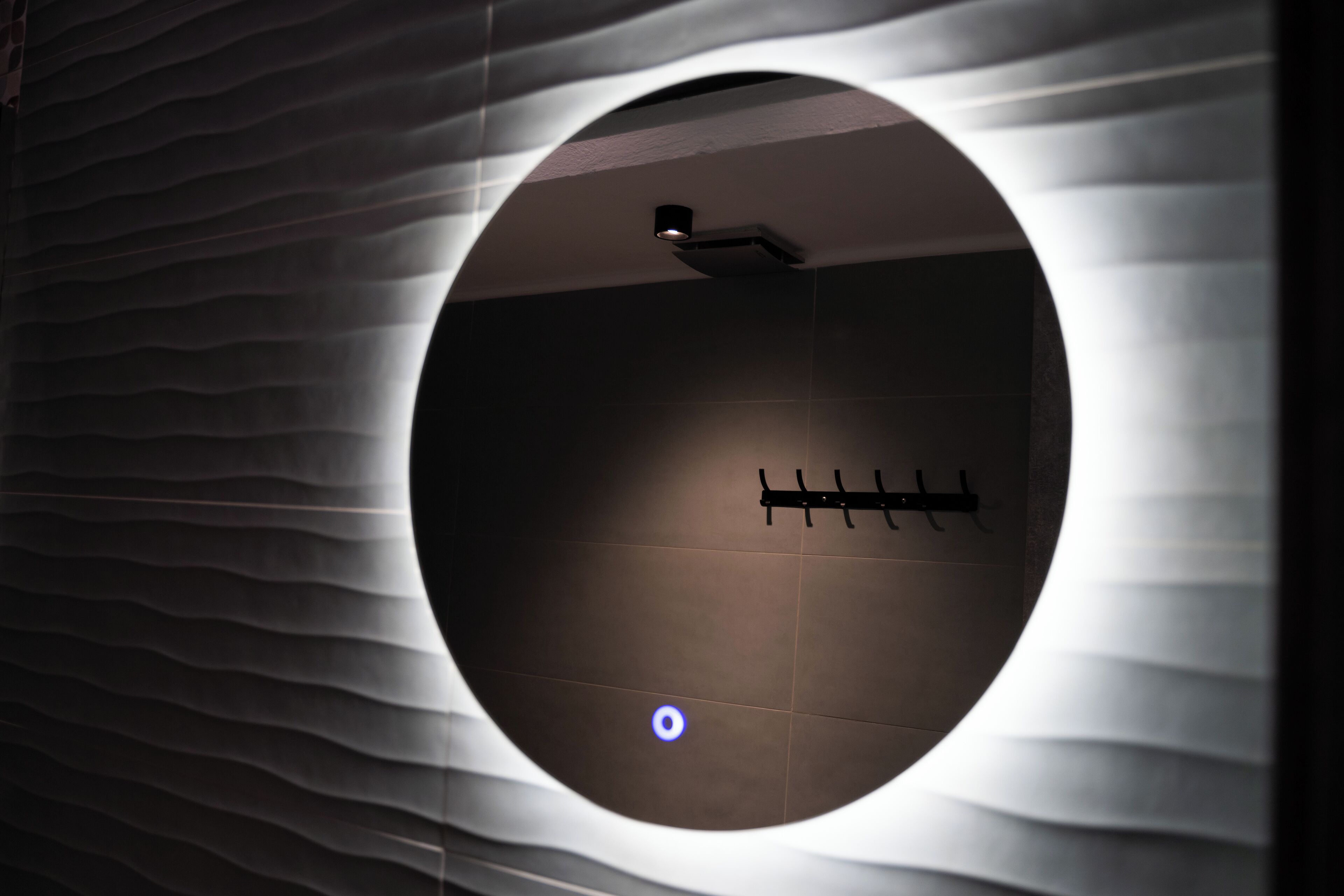A circular window with a wavy pattern on the wall, a light fixture, and a wall-mounted towel rack.