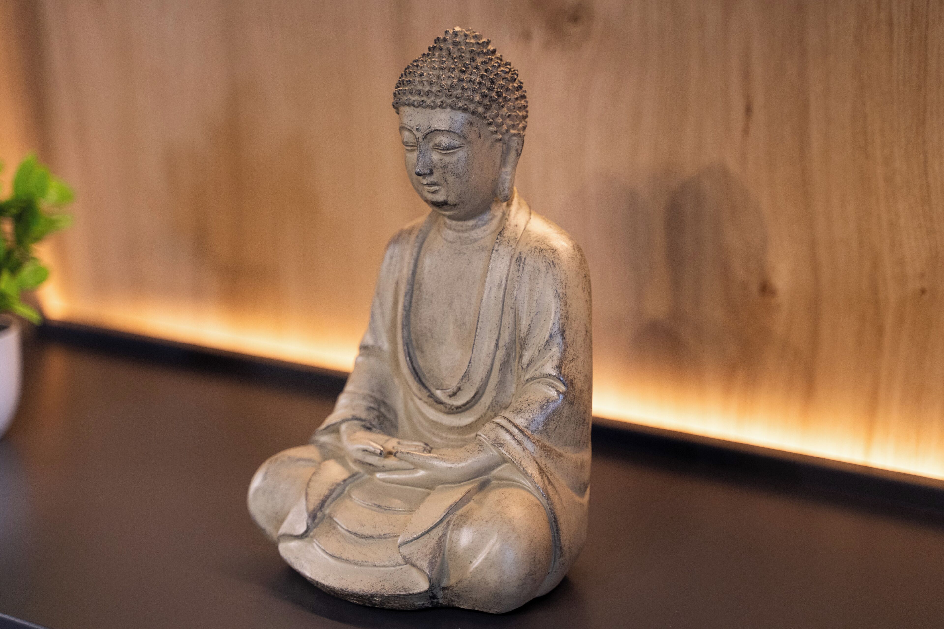 En staty som föreställer en sittande person i en meditativ ställning, placerad på en plan yta med en träbakgrund.