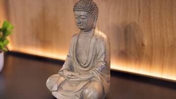 En staty som föreställer en sittande person i en meditativ ställning, placerad på en plan yta med en träbakgrund.