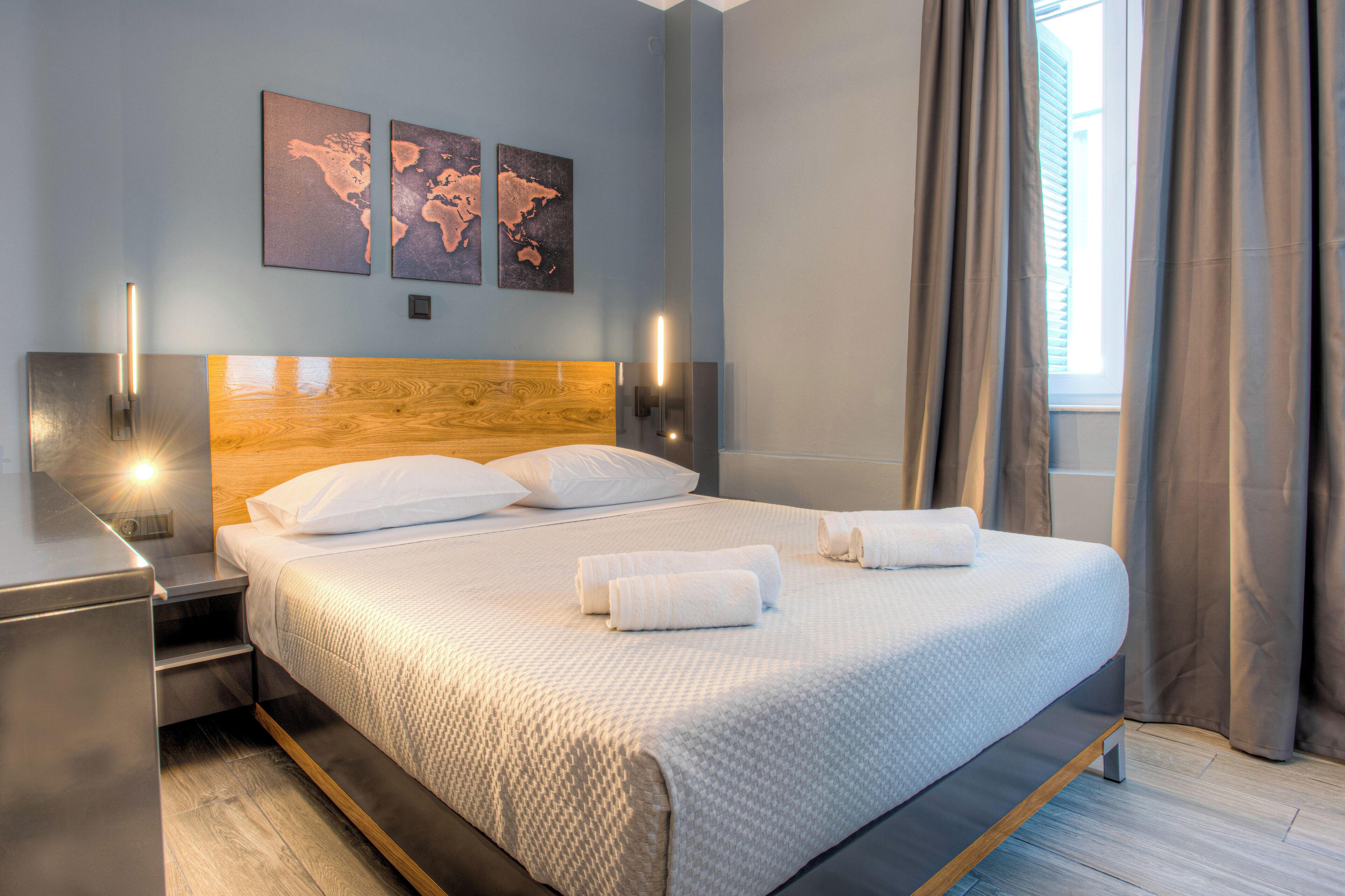 A modern hotel room with a large bed, wooden headboard, and two wall-mounted lights.