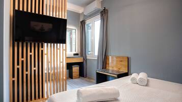 Una habitación de hotel con una cama, un televisor montado en un panel de madera, un escritorio con una silla y una ventana con cortinas.