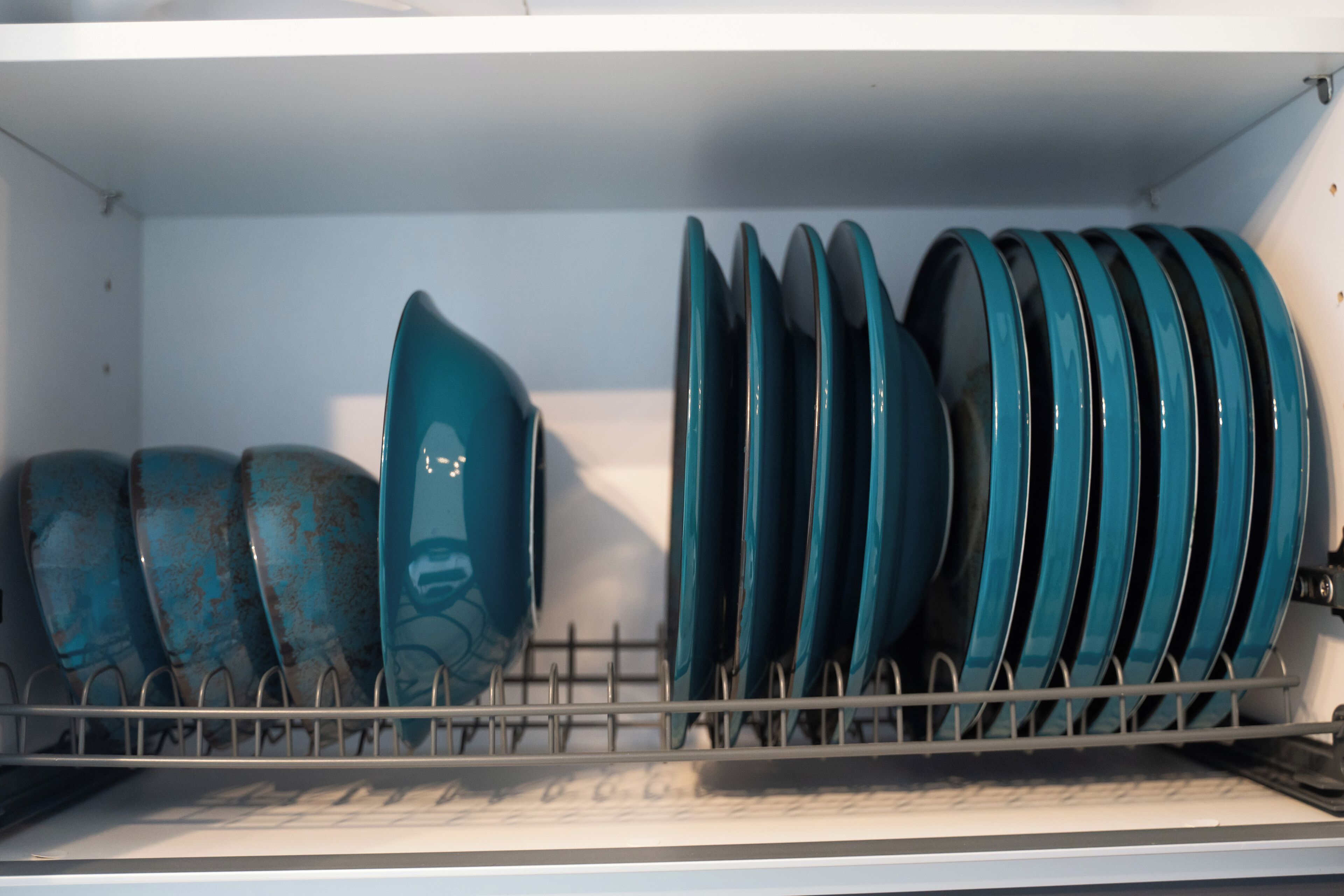 A kitchen with a dish rack holding several blue and green ceramic plates and bowls.