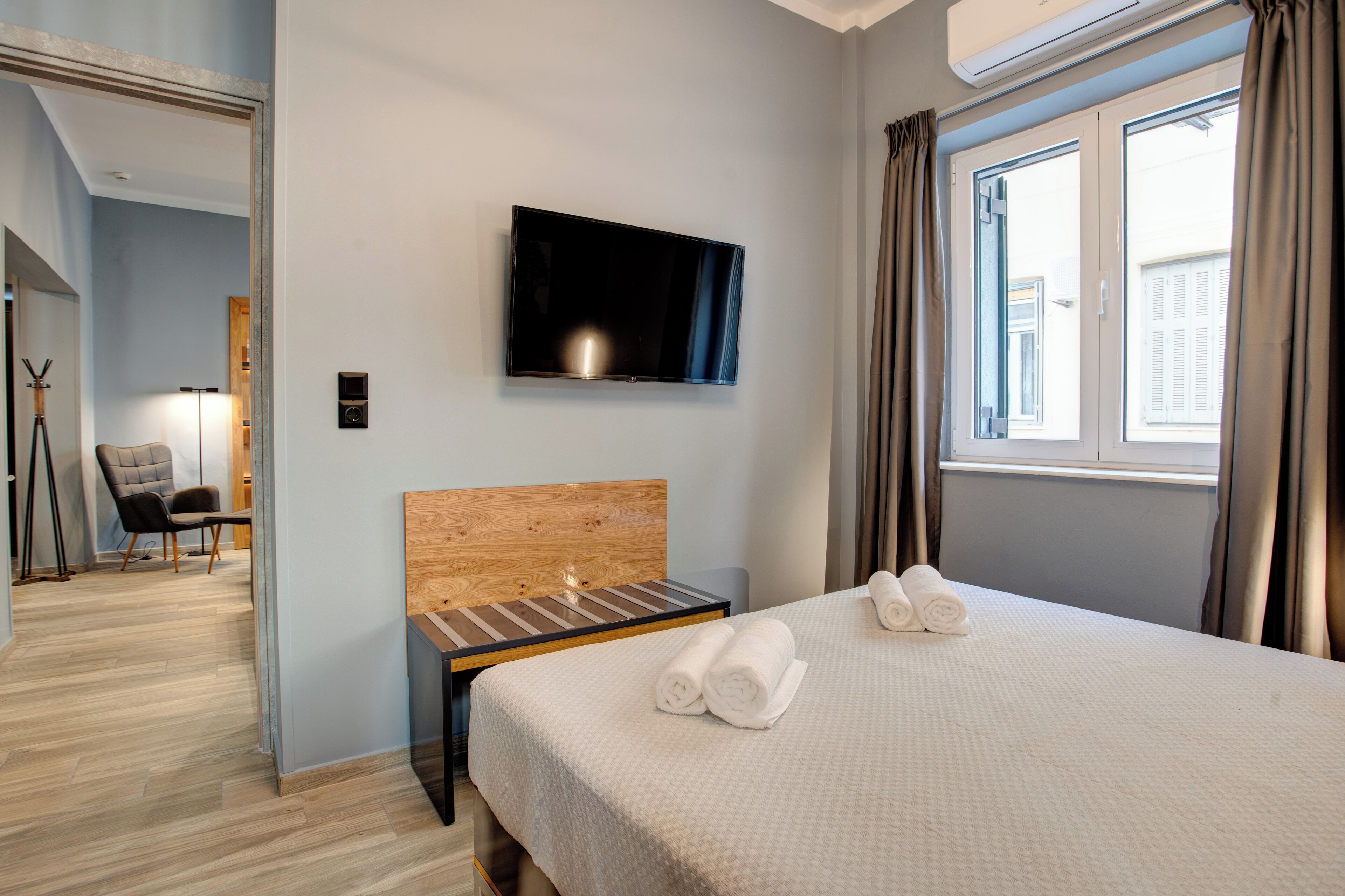 Habitación de hotel con cama, televisor montado en la pared, ventana con cortinas y cabecero de madera.