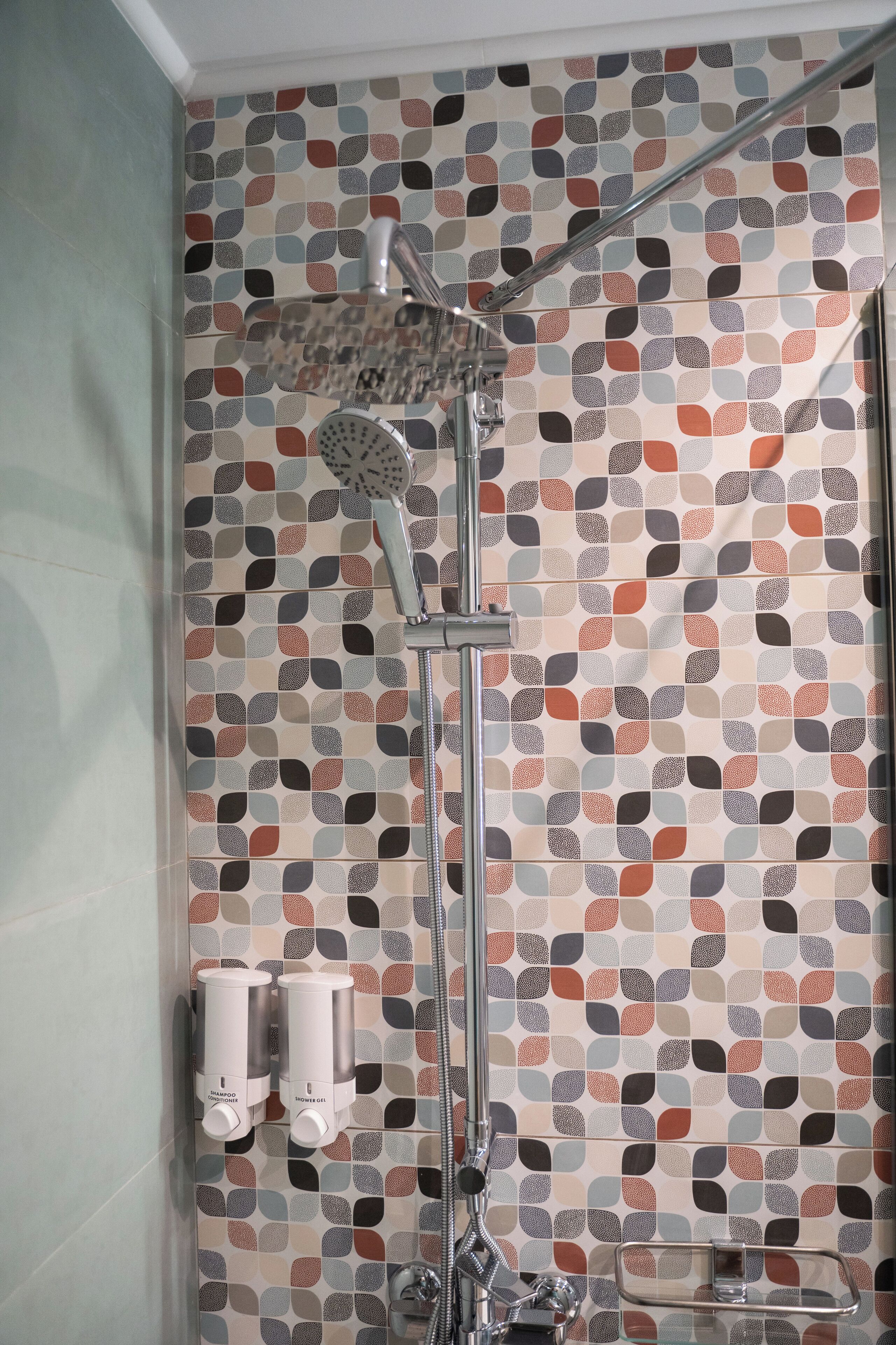 Chuveiro com parede de azulejos estampados, chuveiro manual e dois dispensadores de sabonete.
