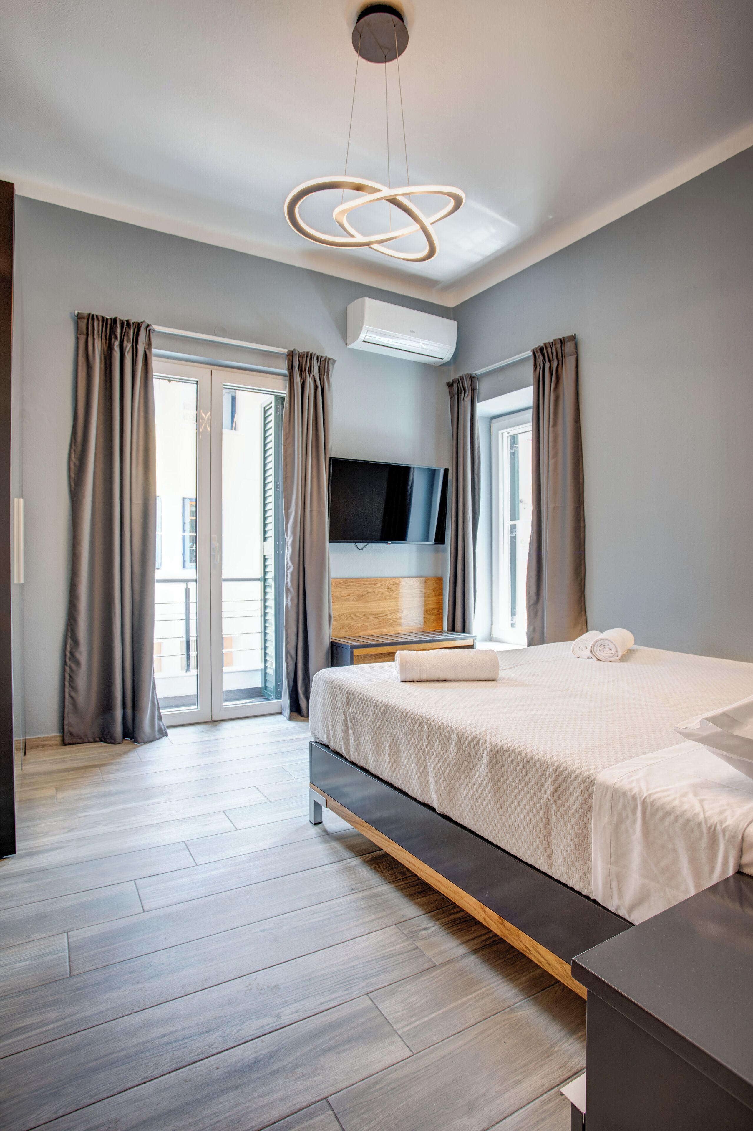 A modern bedroom with a bed, a flat-screen TV, an air conditioner, and a sliding glass door to the outside.