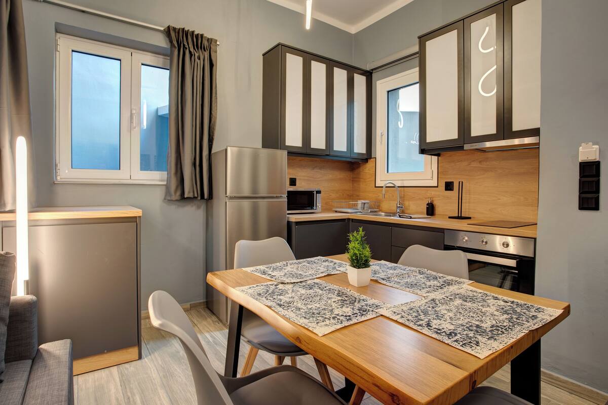 Une cuisine moderne avec des meubles en bois, un four encastré et un coin repas comprenant une table et des chaises en bois.