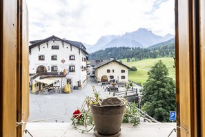 A hotel with a traditional Alpine architectural style, featuring a courtyard with outdoor seating and a mountain view.