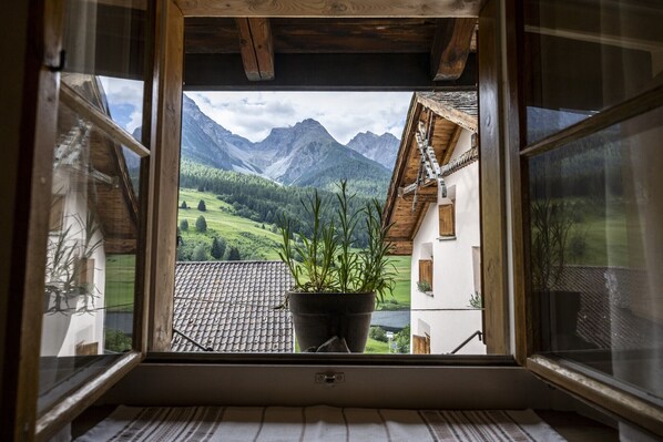 A window view of a mountain landscape with a potted plant on the windowsill.