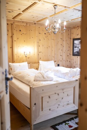A wooden-paneled bedroom with a bed, a chandelier, and a wall-mounted light fixture.