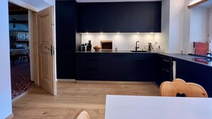 Eine moderne Küche mit dunklen Schränken, einem Holztisch und einem sichtbaren Durchgang zu einem anderen Raum.