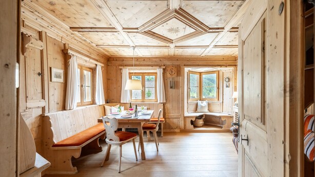 Ein Holzblockbau-Innenraum mit Essbereich, Bänken und Blick ins Freie.