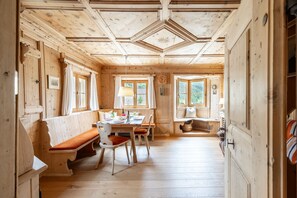 A wooden cabin interior with a dining area, benches, and a view of the outdoors.