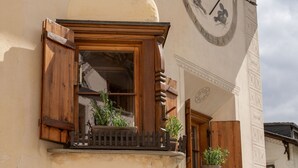 Ein Gebäude mit einer großen Uhr, hölzernen Rollläden und Pflanzenkübeln am Balkon.