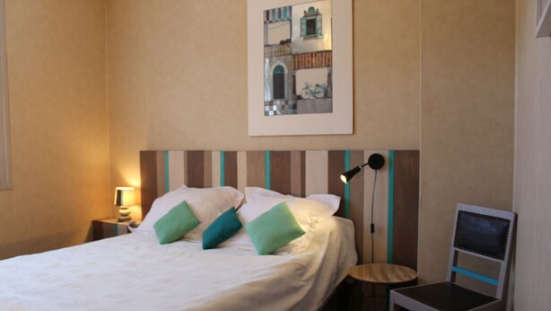 A neatly made bed with white bedding and green pillows, a bedside lamp, a chair, and a framed picture on the wall. - House with garden in the heart of the village of Gerde. Pets allowed. (Gerde)