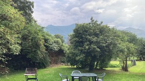 A grassy outdoor area with a table and chairs, surrounded by trees and a view of distant mountains. - House with garden in the heart of the village of Gerde. Pets allowed. (Gerde)
