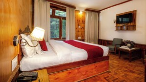 A wooden-framed bed with white and red bedding, a bedside lamp, a telephone, and a TV mounted on the wall. - Vivaan Stay Holiday Home international (Manali)