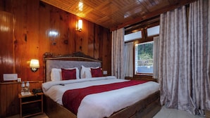 A wooden-paneled bedroom with a large bed, a nightstand, and a window with curtains. - Vivaan Stay Holiday Home international (Manali)