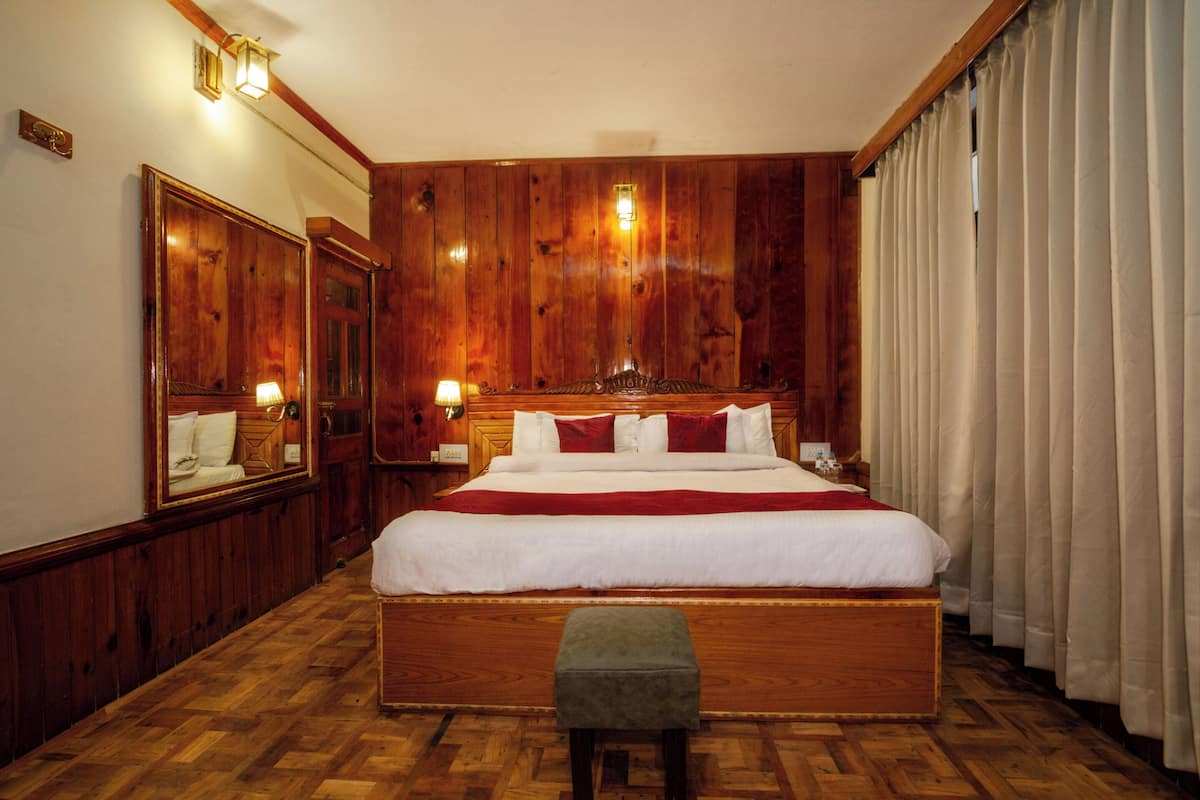 Habitación de hotel con una cama grande, paneles de madera, un banco y un espejo.