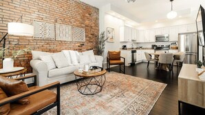 A modern kitchen with white cabinets, stainless steel appliances, and a brick accent wall. - 4BR House | City Views | Balconies | Walk to OTR (Cincinnati)