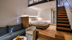 Een moderne slaapkamer met een bed, een bank, een stoel, een klein tafeltje met fruit en een houten trap.