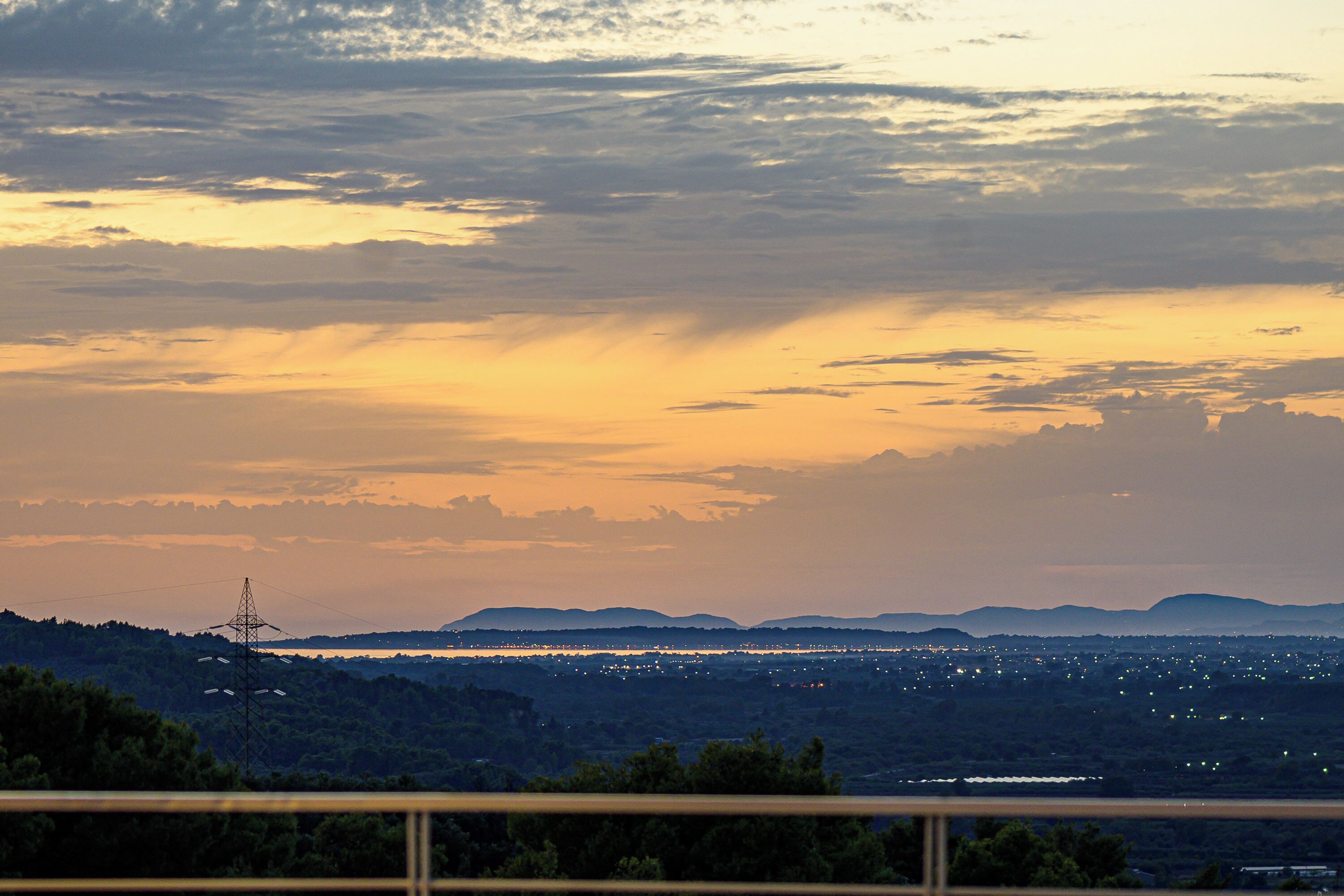 A sunset view over a city with distant mountains and a power line tower.