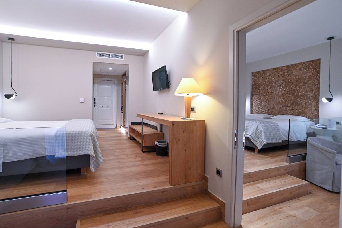 Moderni hotellihuone, jossa on kaksi sänkyä, puinen työpöytä, televisio ja lamppu.