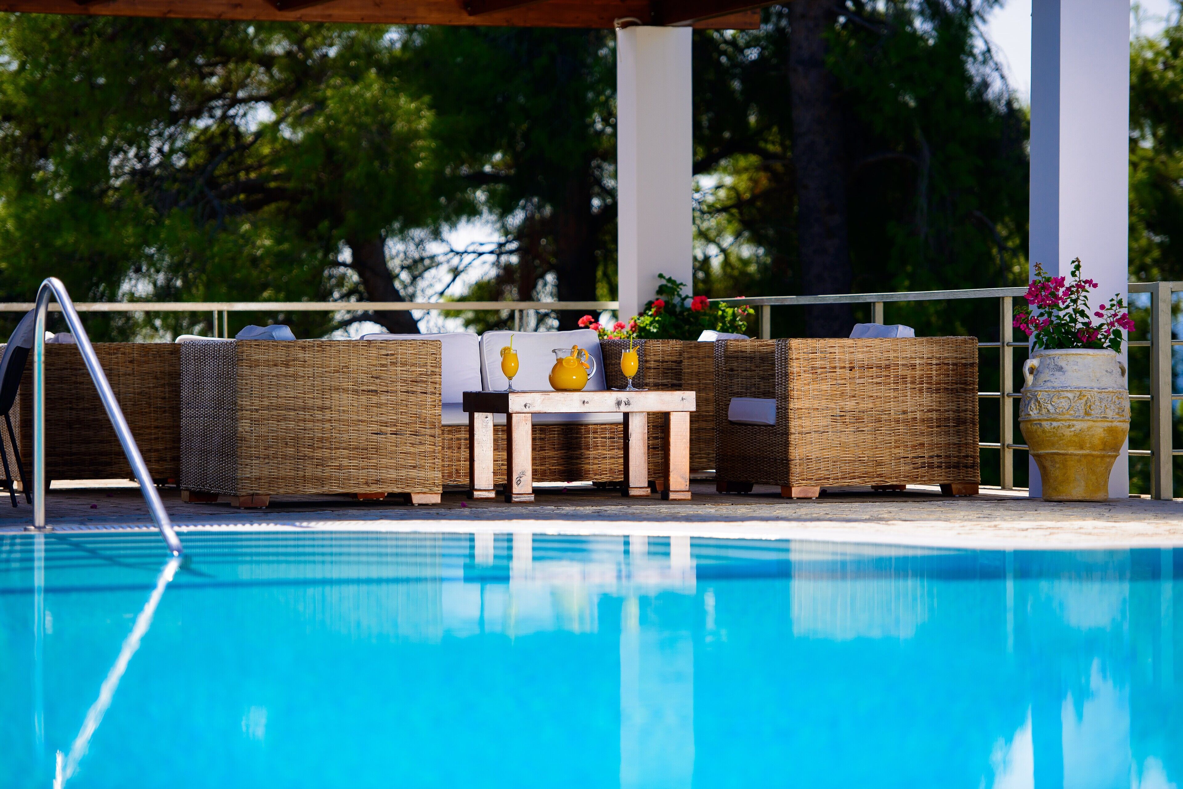 A poolside area with wicker furniture, a table, and a potted plant.