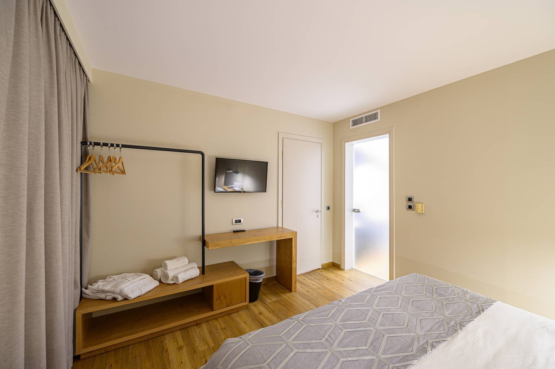 A hotel room with a bed, a wooden nightstand with towels, a TV, and a door.