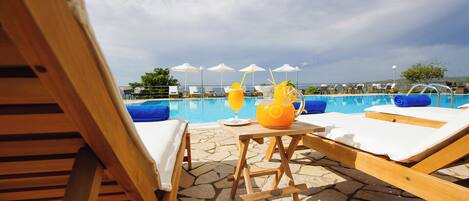 Zona de piscina con sillones de descanso, una mesa con bebidas y vistas a la piscina.