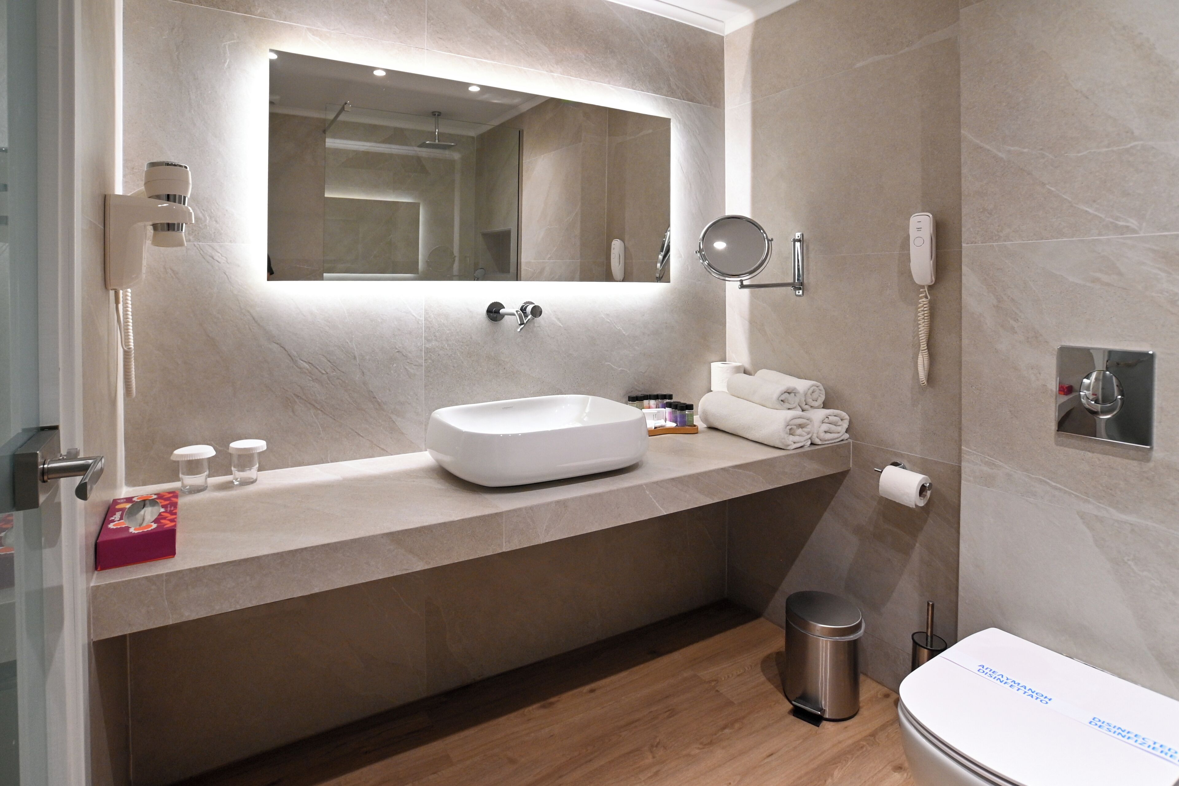 Une salle de bain moderne avec un grand miroir, un lavabo encastré, des toilettes et une poubelle.