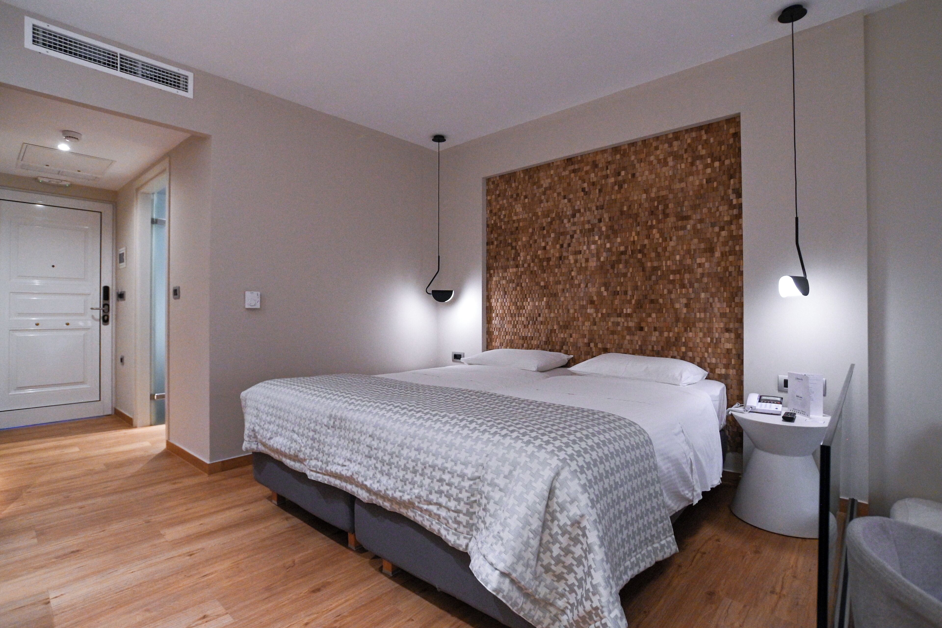 Un dormitorio con una cama grande, mesitas de noche, un calentador en la pared y piso de madera.