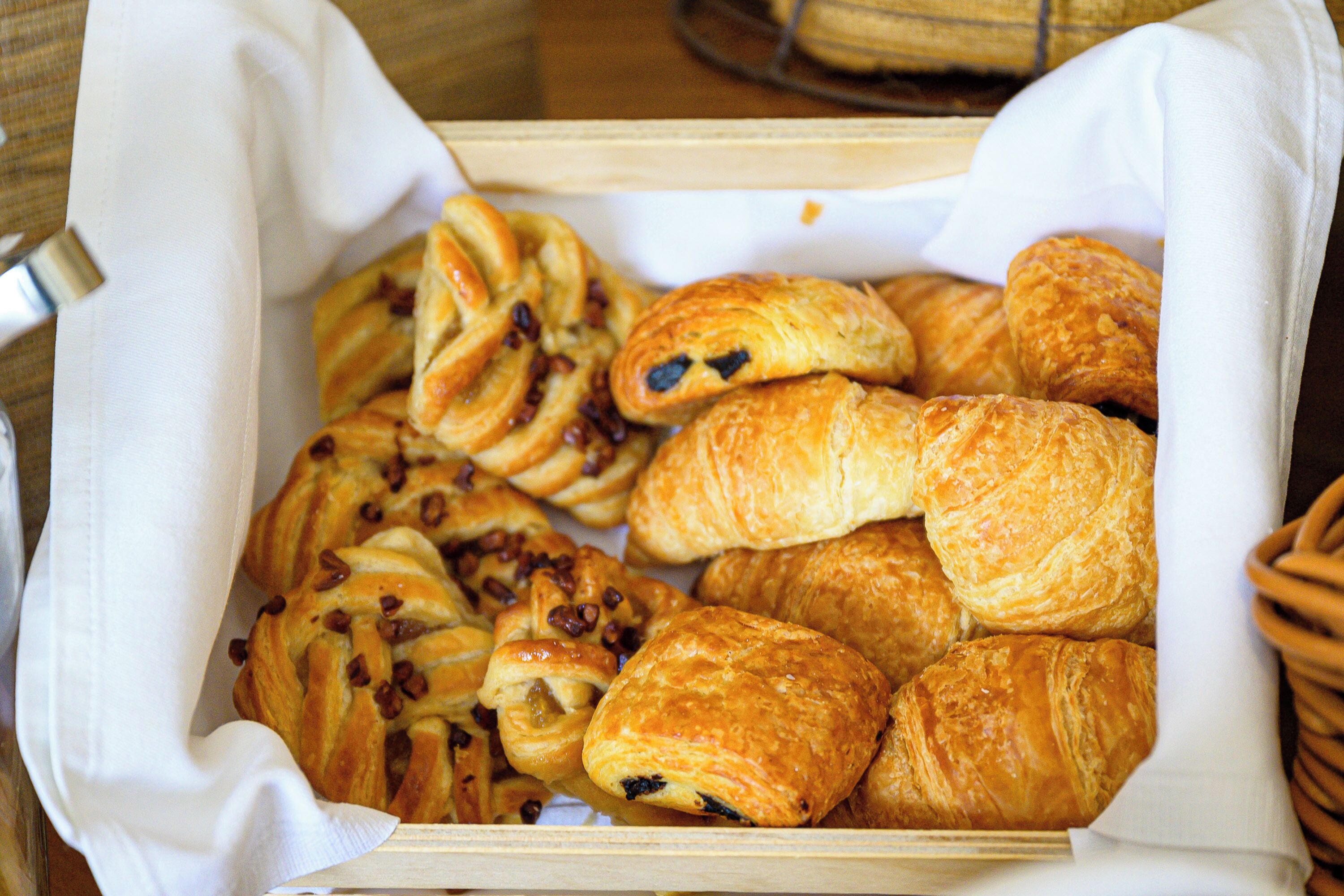 A wooden box filled with various pastries, including croissants and rolls, placed on a table.