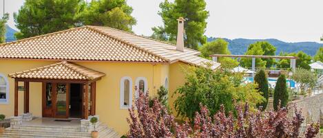 A yellow building with a tiled roof, a covered porch, and a stone pathway leading to the entrance.