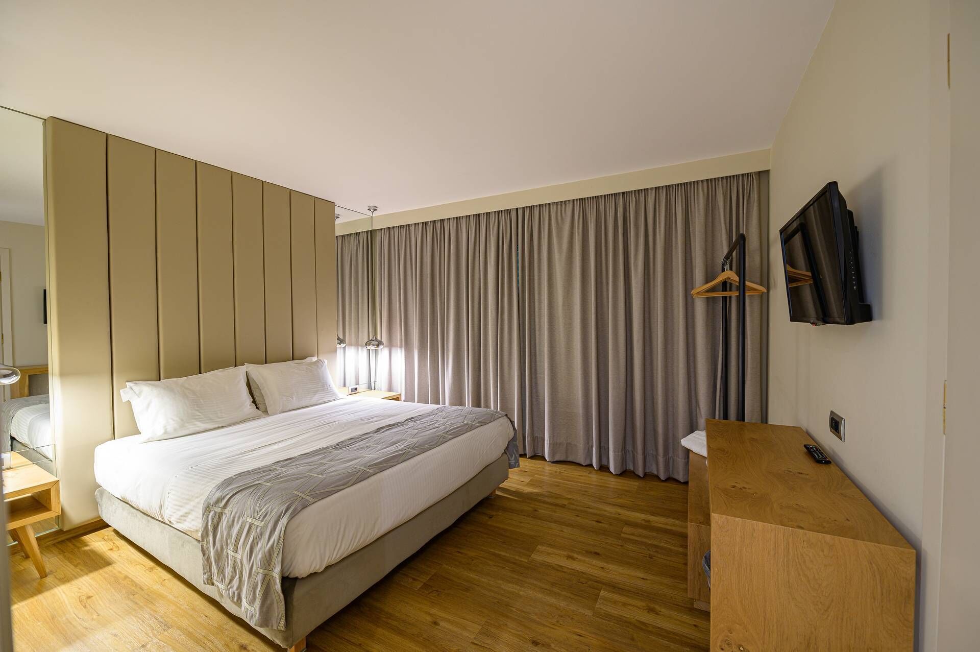 A modern hotel room with a large bed, wooden flooring, a TV, and a wardrobe.